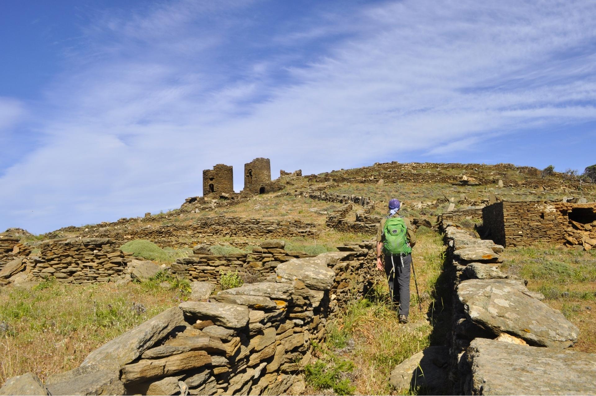 A hiker walks between ancient stone walls on a traditional mule path in Tinos.