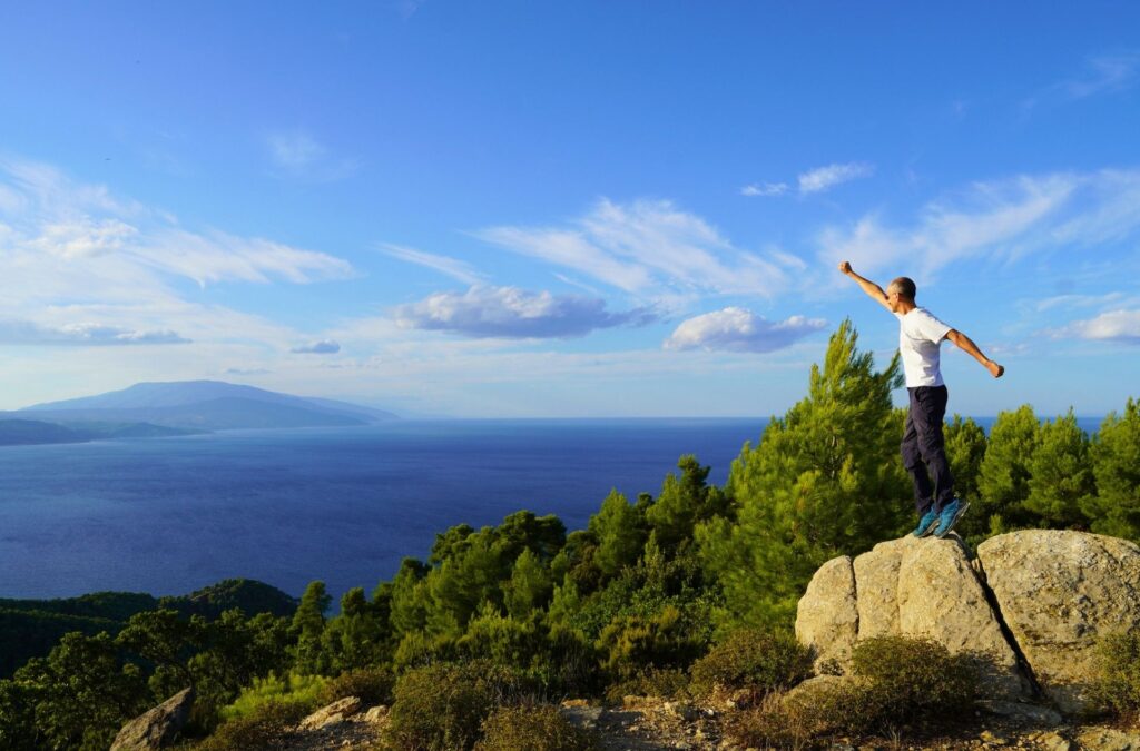 A hiker on a forested summit with sea at the background