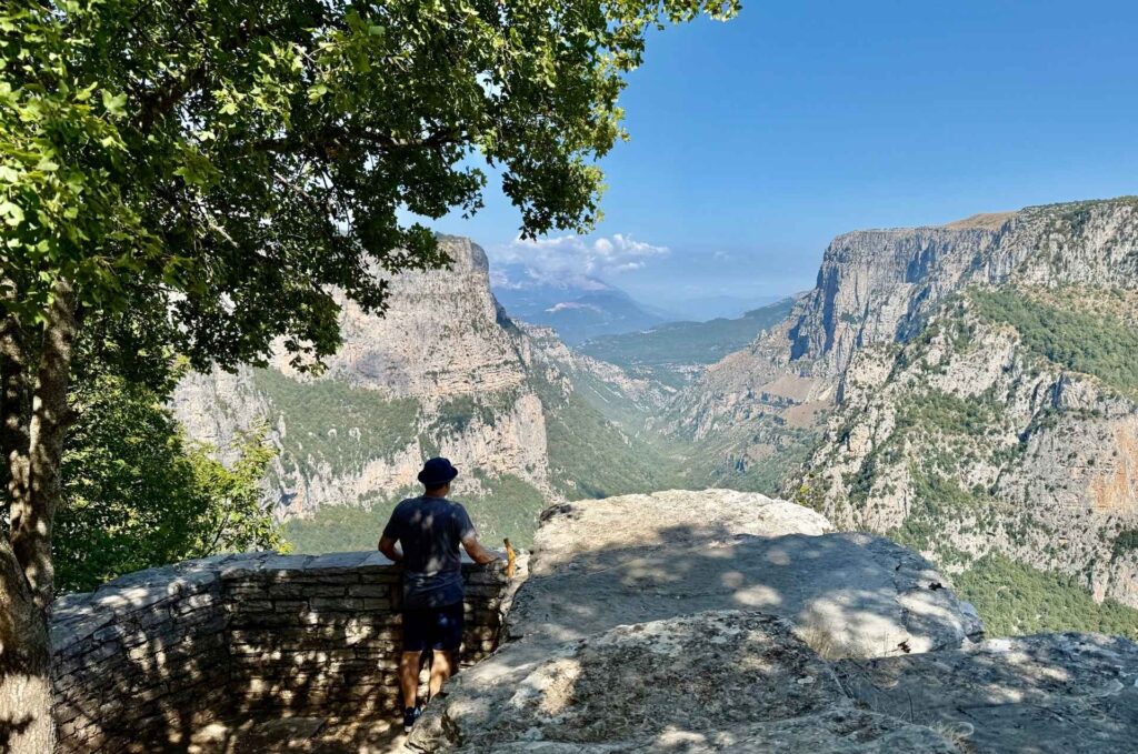A hiker admiring the monumental scale of the Vikos Gorge from the Beloi lookout.
