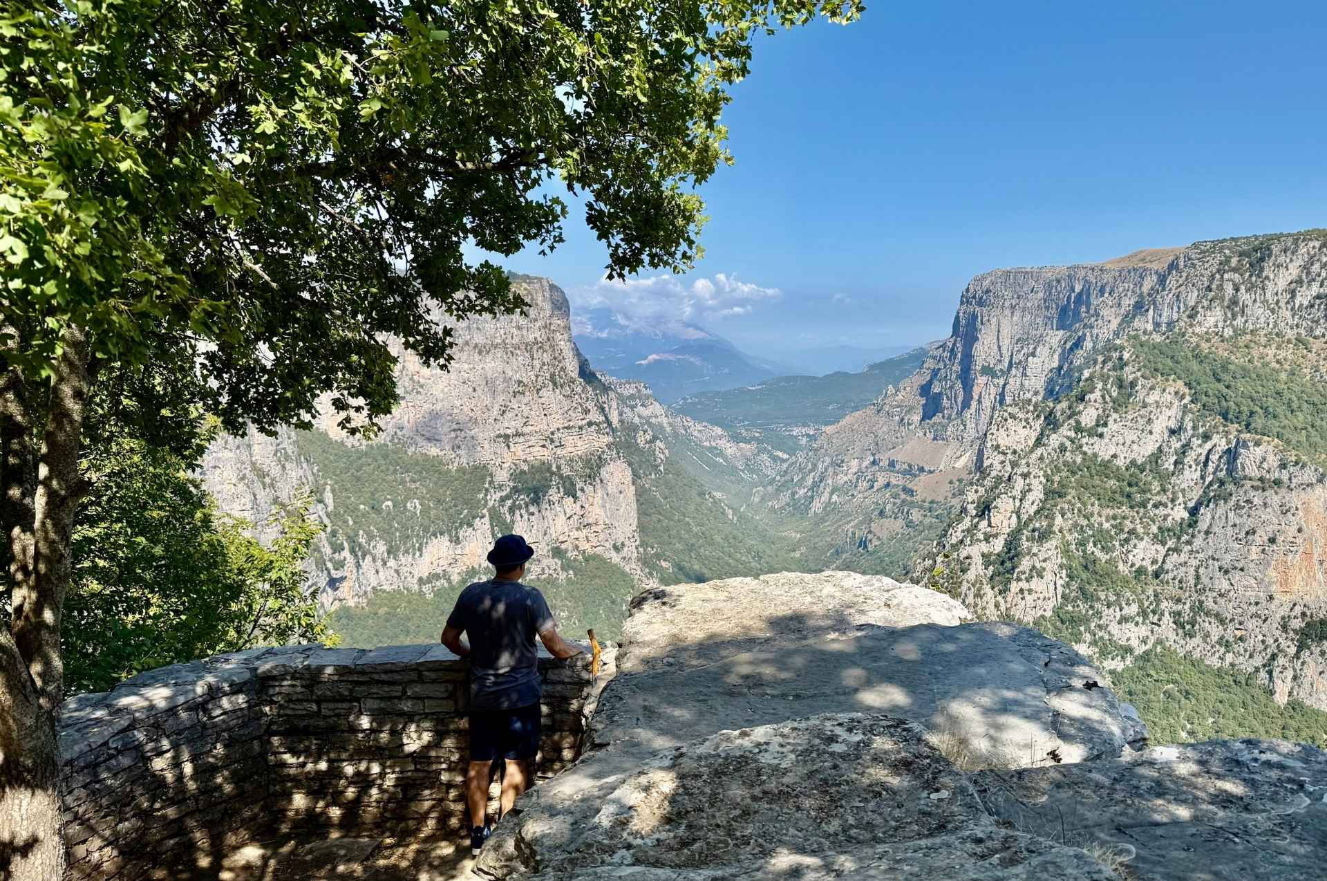 A hiker admiring the monumental scale of the Vikos Gorge from the Beloi lookout.