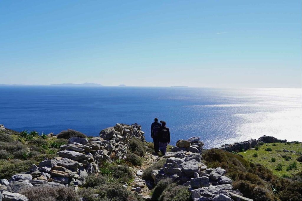 Hikers descending an ancient stone kalderimi overlooking the deep Aegean Sea in Amorgos - Hike Greece