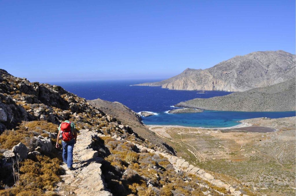 Hiker navigating a rugged stone path along the dramatic coastline of Karpathos - Hike Greece