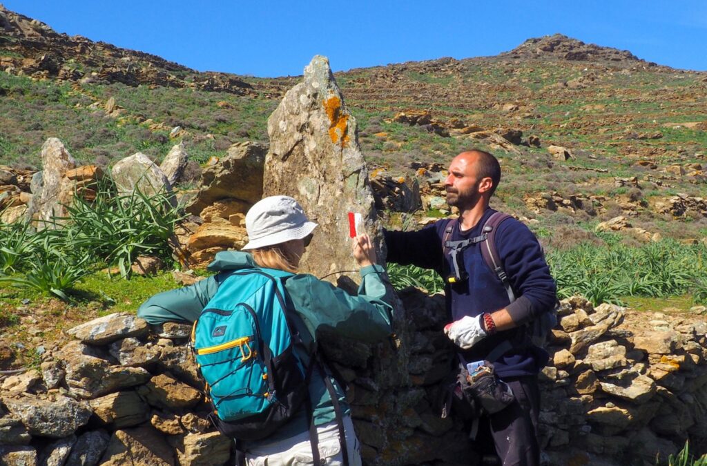 Field team member from Paths of Greece painting a trail waymarker on a stone wall in Tinos - Hike Greece