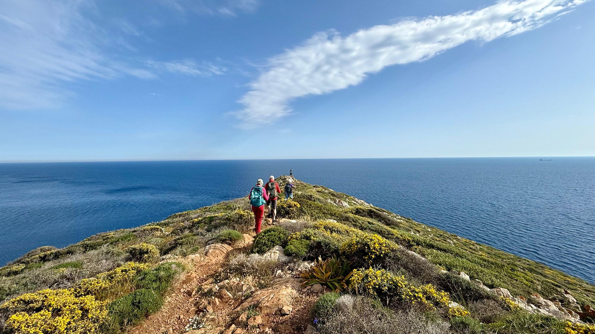 Hikers walking along a grassy headland above the sea near Cape Tainaro in the Mani, Peloponnese