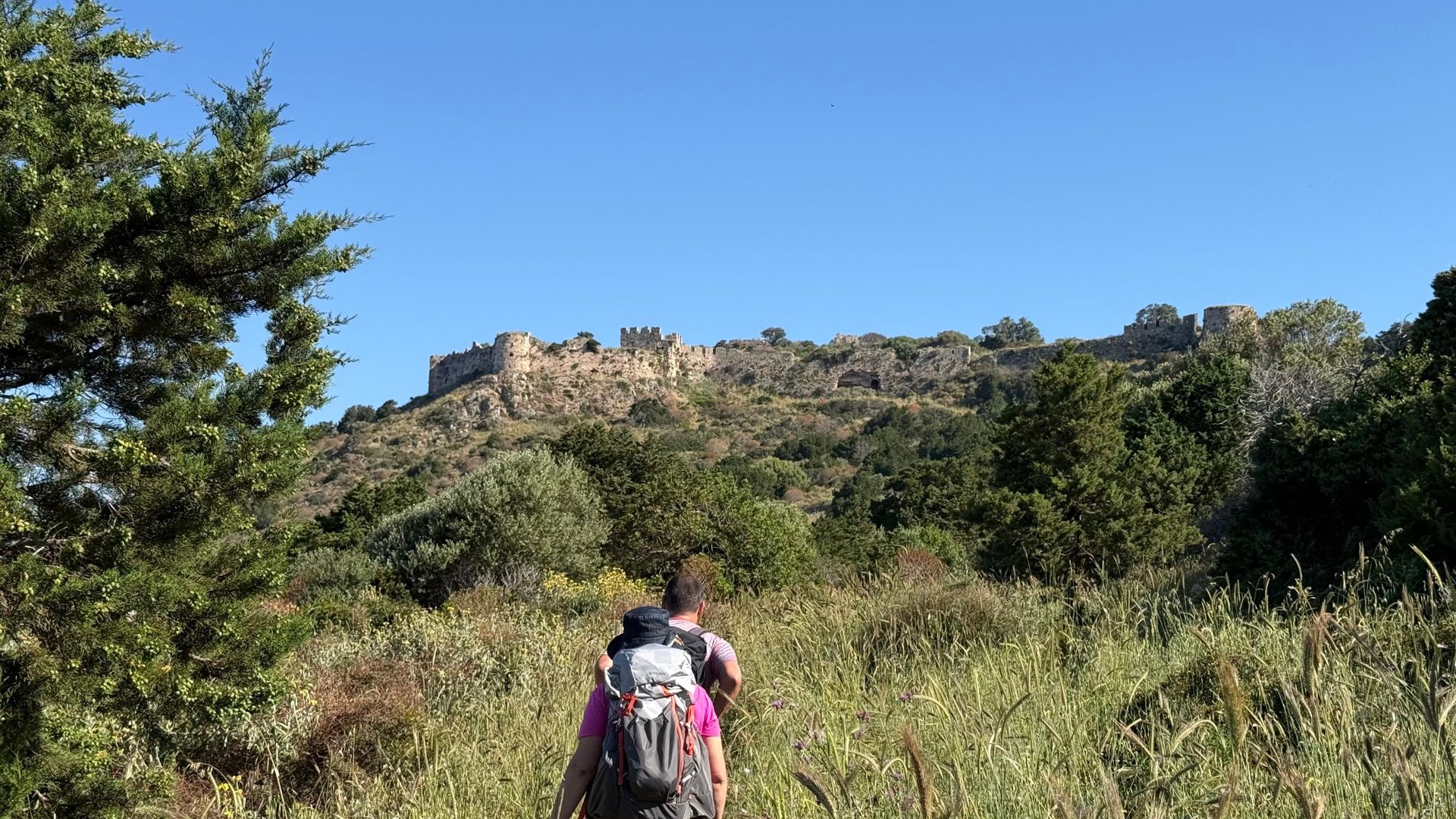 Hiker walking towards a medieval fortress on a hill in the Peloponnese